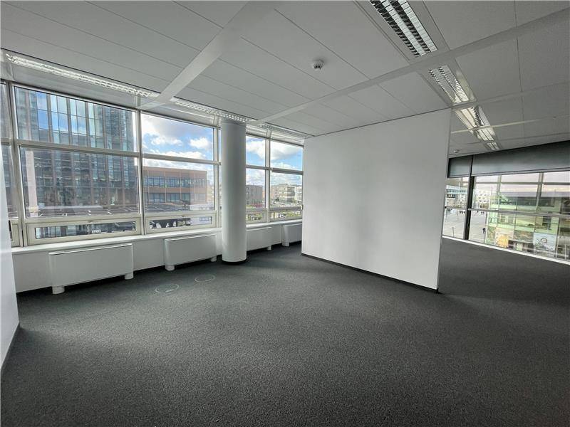 Geräumiges, unmöbliertes Büro mit Teppichboden und großen Fenstern, die viel Tageslicht und einen Blick nach draußen bieten.
