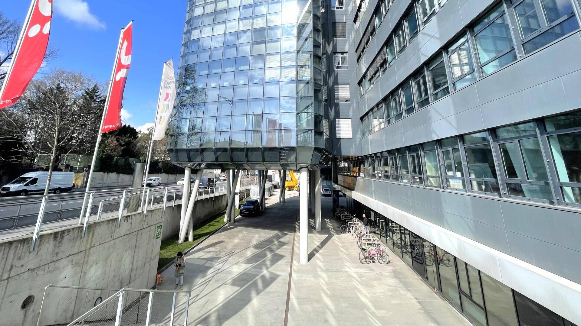 Moderne Bürogebäude-Fassade mit Glas- und Metallverkleidung, umgeben von einer Straße und Grünflächen.
