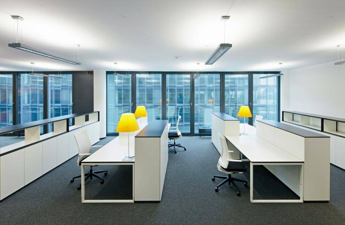 Geräumiges Großraumbüro mit ergonomischen Bürostühlen, modernen Möbeln und Teppichboden.