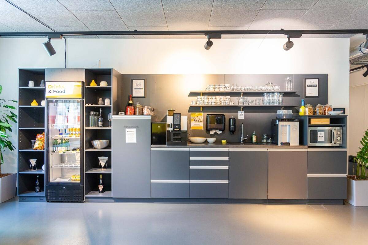 Moderne Teeküche in einem Büro mit integrierten Geräten, Kühlschrank und Regalen für Geschirr.