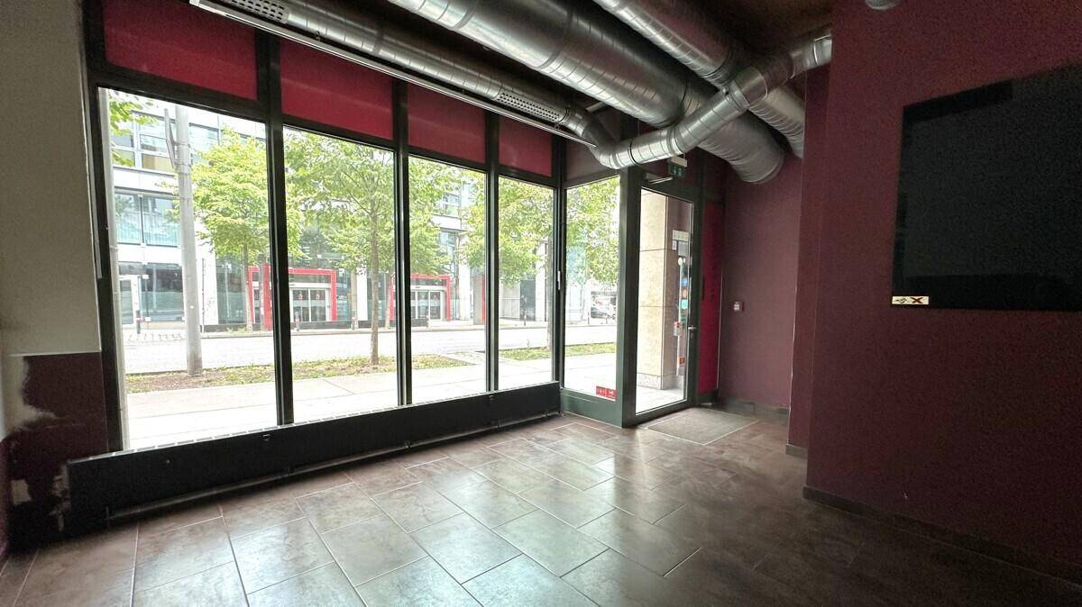 Leerer Geschäftsraum mit großen Schaufenstern, Blick auf die Straße und sichtbaren Lüftungsrohren an der Decke.