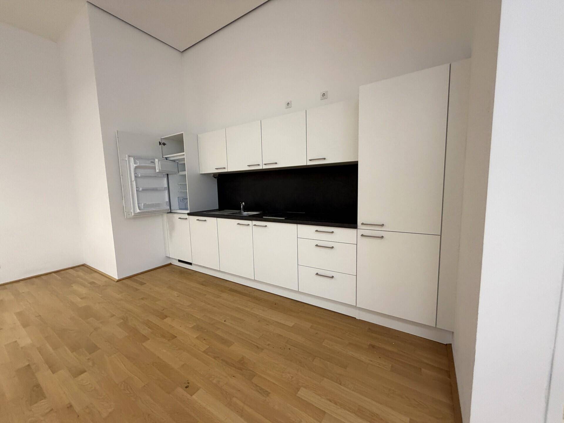 Moderne Küchenzeile mit weißen Schränken, schwarzer Arbeitsplatte und integriertem Kühlschrank.