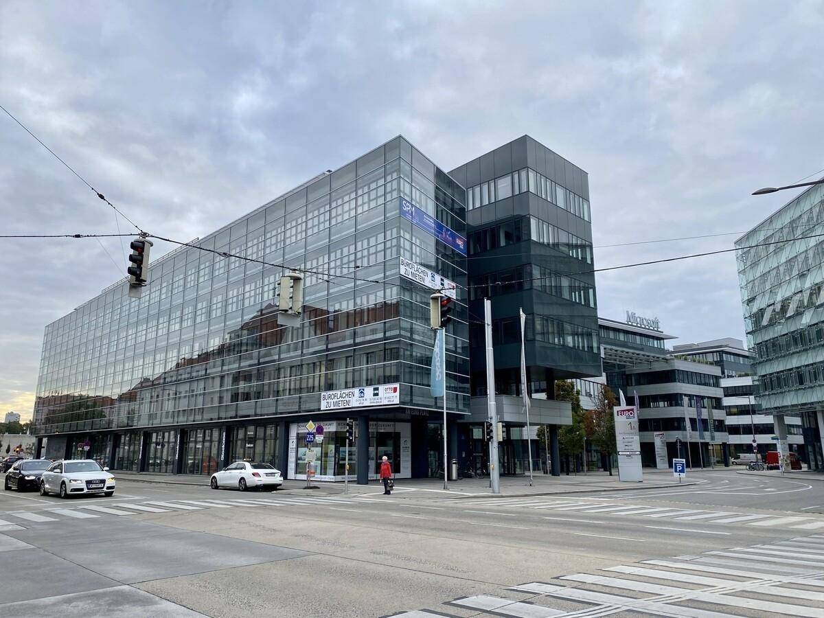Großes Bürogebäude an einer Straßenecke mit moderner Glasfassade und viel Tageslicht, umgeben von Stadtverkehr.