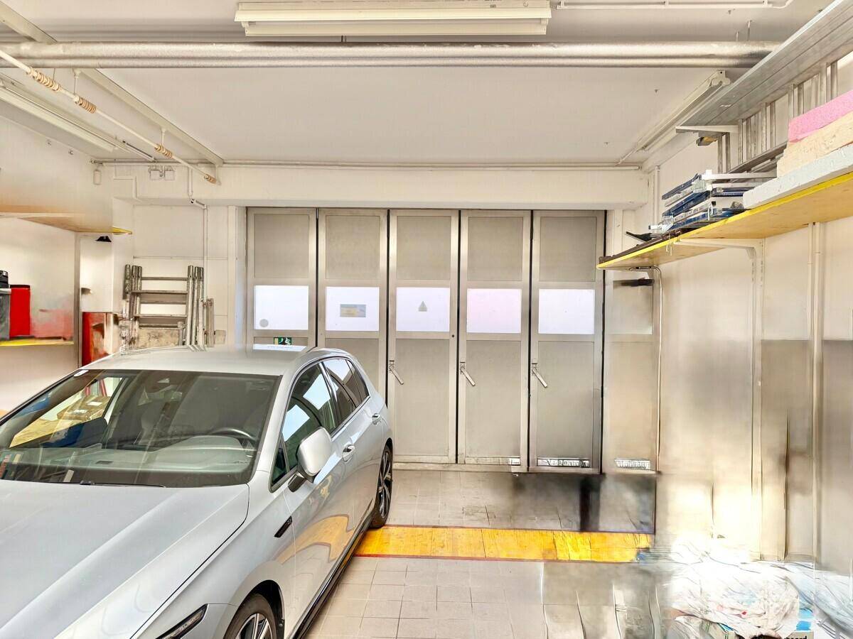 Geräumige Garage mit einem geparkten Auto, großen Falttoren und sichtbaren Leitungen an der Decke.