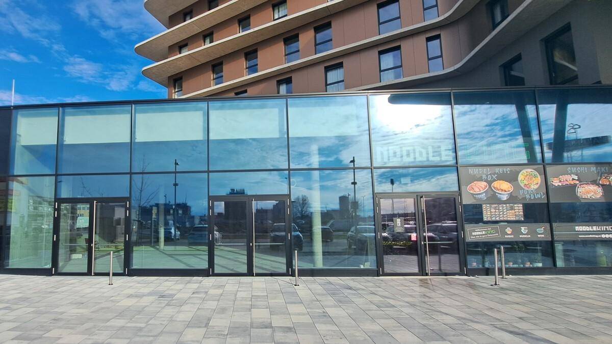 Moderne Glasfassade des Erdgeschosses mit großen Schaufenstern und Werbeschildern für ein Restaurant.