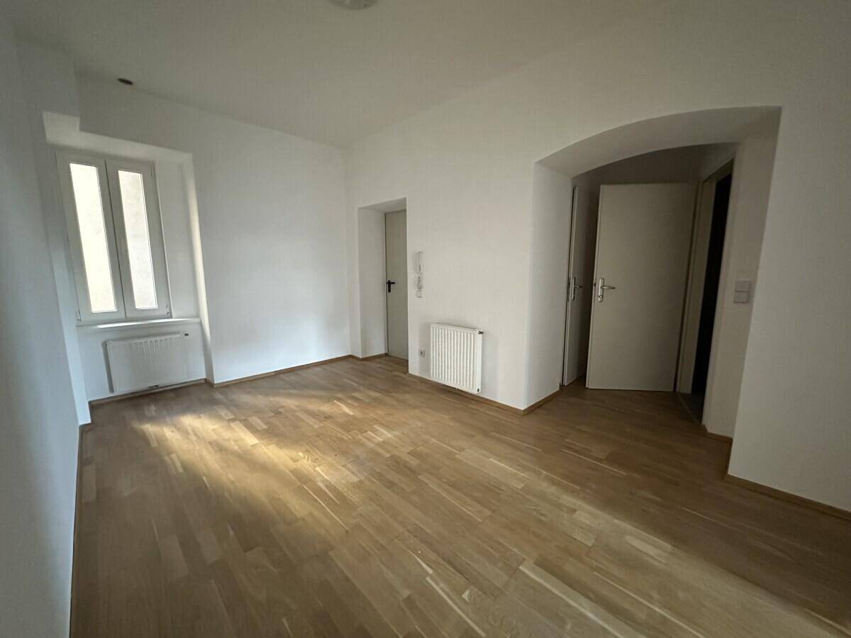 Büroraum mit hellem Parkettboden, weißen Wänden und einem Fenster, das Tageslicht hereinlässt.