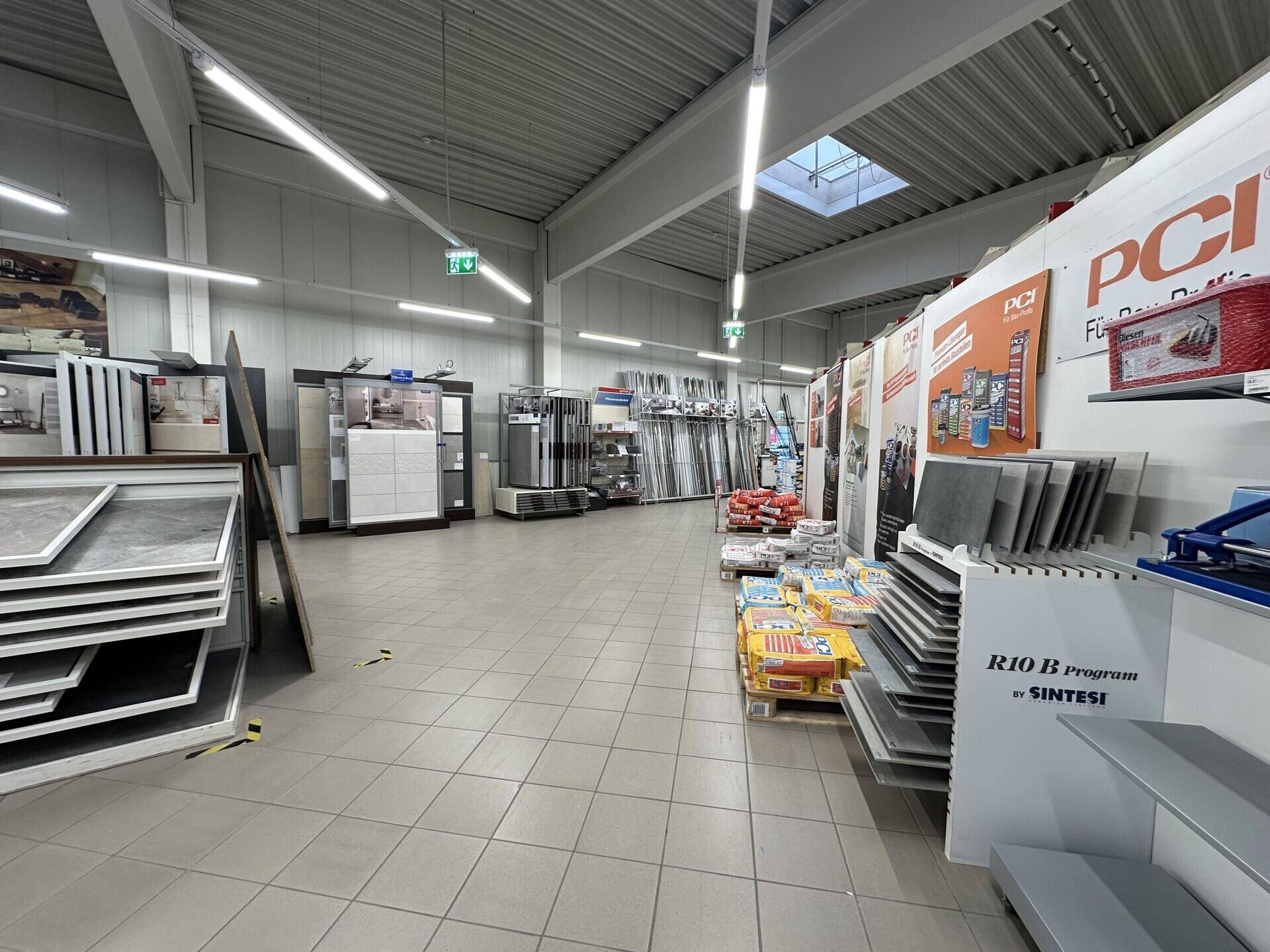 Gang im Baumarkt mit zahlreichen Fliesen- und Baumaterialauslagen unter heller Deckenbeleuchtung.