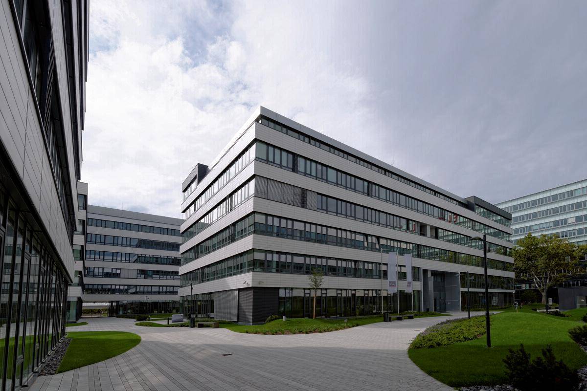 Moderne Bürogebäude mit großen Fensterfronten und gepflegten Grünflächen, die eine angenehme Arbeitsumgebung schaffen.