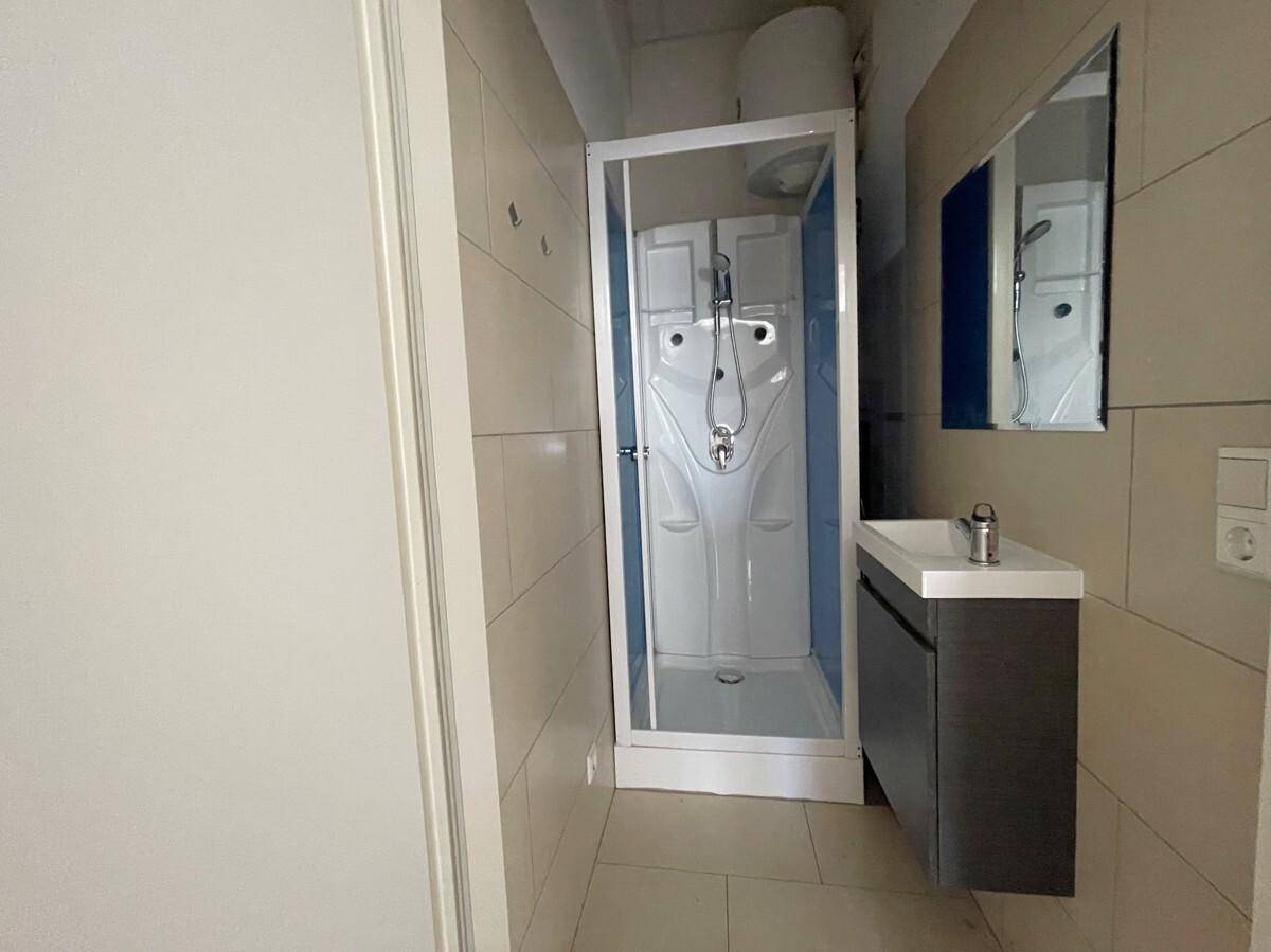 Kleines Badezimmer mit Duschkabine, Waschbecken mit Unterschrank und einem Spiegel.