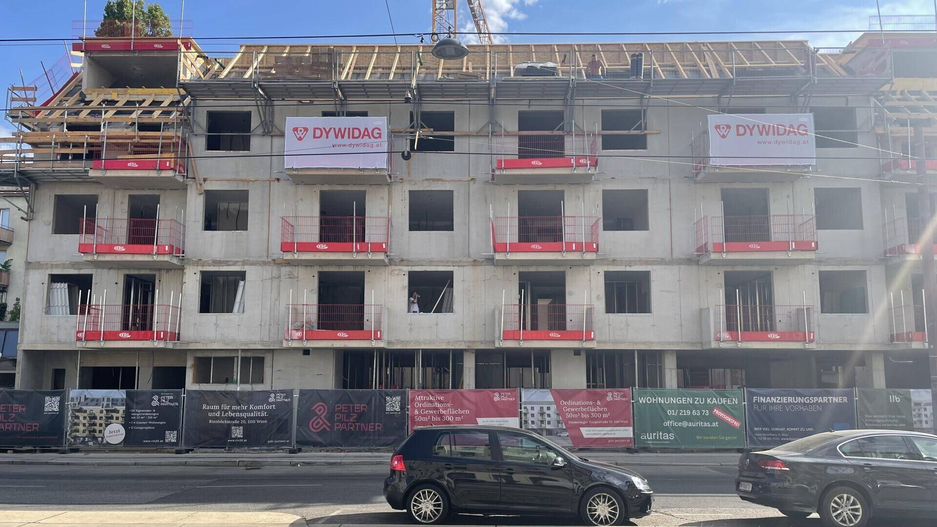 Baustelle eines Mehrfamilienhauses mit sichtbarer Betonstruktur und Baugerüst an einem sonnigen Tag.