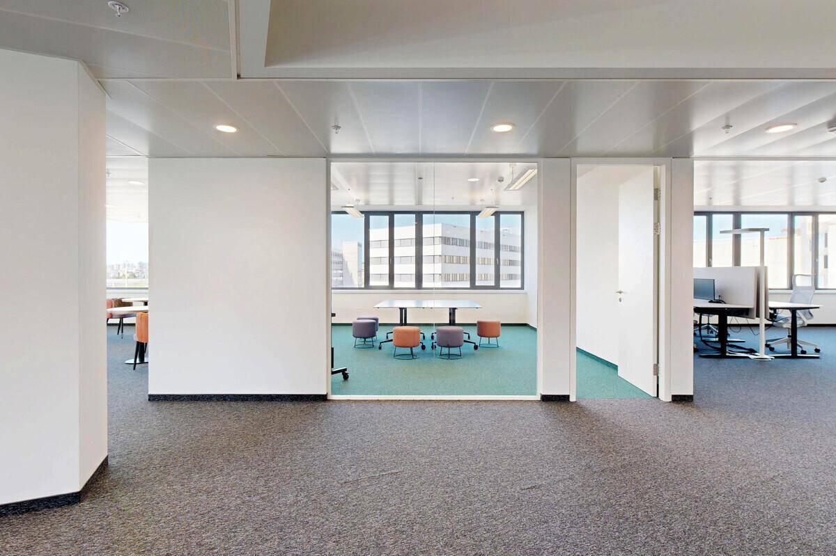 Heller Bürogang mit Teppichboden, der zu verschiedenen Büroräumen und Besprechungsbereichen führt.