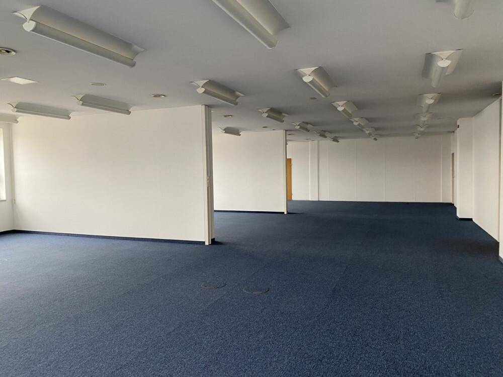 Großer, leerer Büroraum mit blauem Teppichboden und weißen Wänden, ideal für flexible Nutzung.