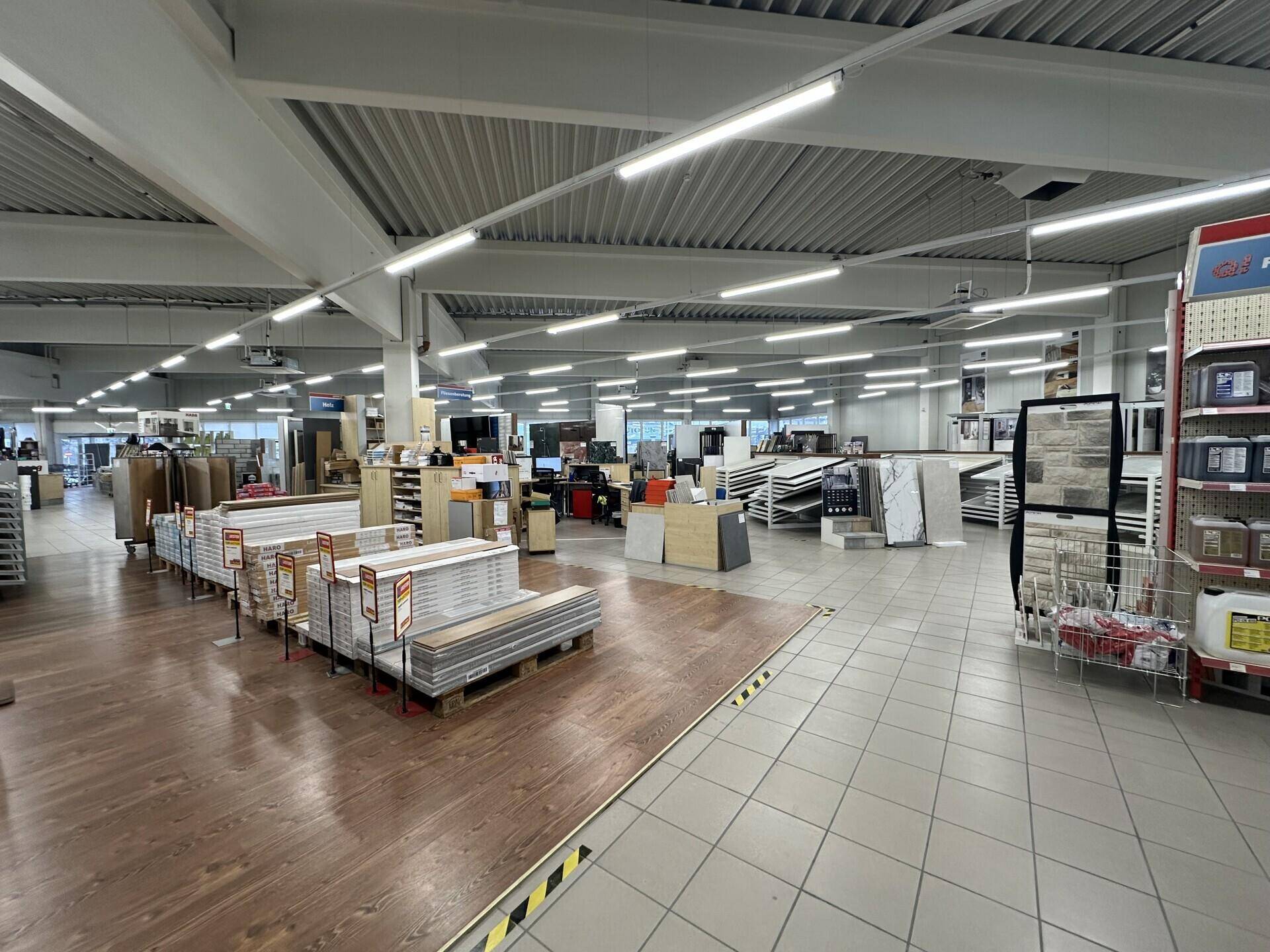 Verkaufsbereich mit Auslagen für Bodenbeläge und Fliesen, teilweise mit Holzoptik-Laminat.