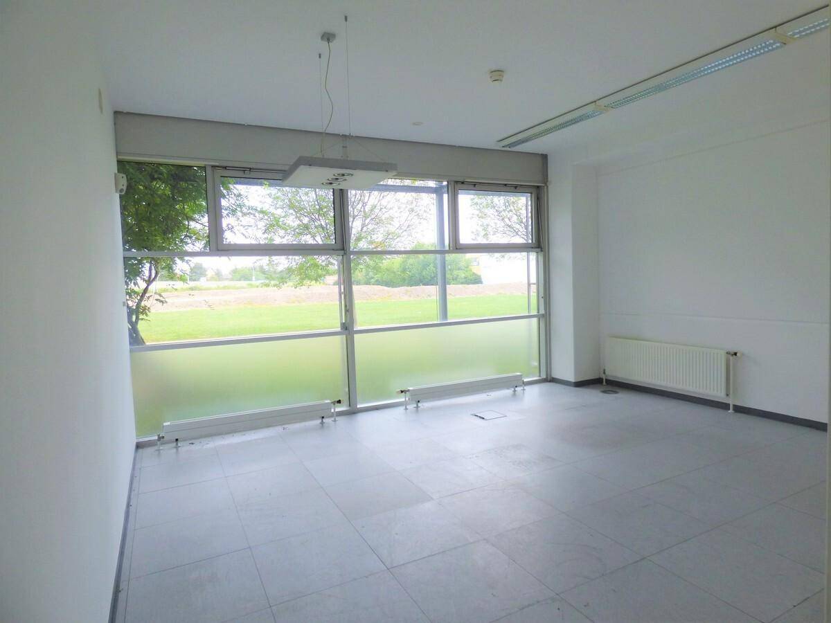 Helles, leeres Büro mit großen Fenstern, die einen Blick ins Grüne bieten, und Fliesenboden.