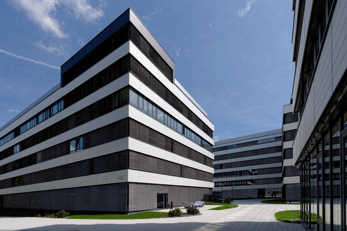 Mehrere moderne Bürogebäude mit klaren Linien und großen Fenstern, umgeben von gepflegten Außenanlagen.