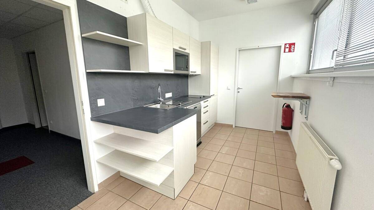 Funktionale Küchenzeile mit hellen Schränken, Spüle, Mikrowelle und Fliesenboden in einem Bürobereich.