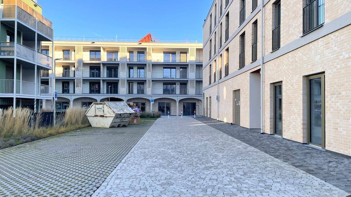 Außenbereich zwischen zwei modernen Neubauten mit gepflastertem Hof und Baustellencontainer.