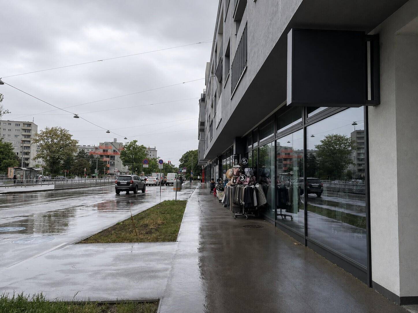 Seitenansicht eines modernen Gebäudes mit großen Schaufenstern und einer nassen Straße im Vordergrund.