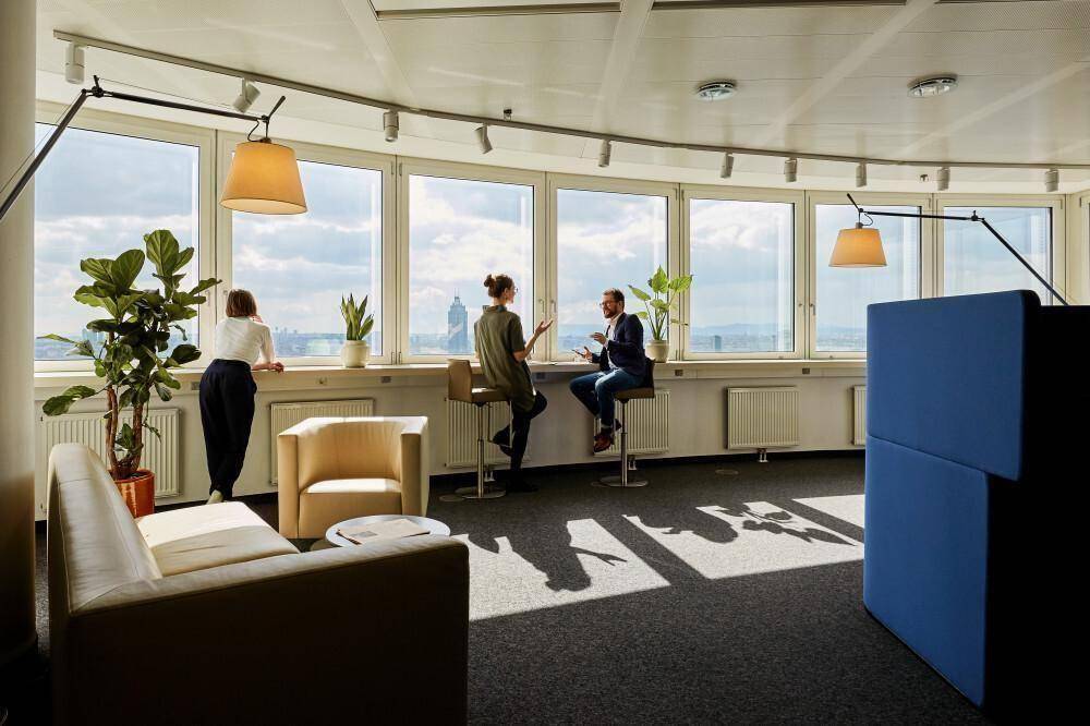 Heller Bürobereich mit großen Fenstern, die einen weiten Blick über die Stadt bieten, und modernen Sitzgelegenheiten.