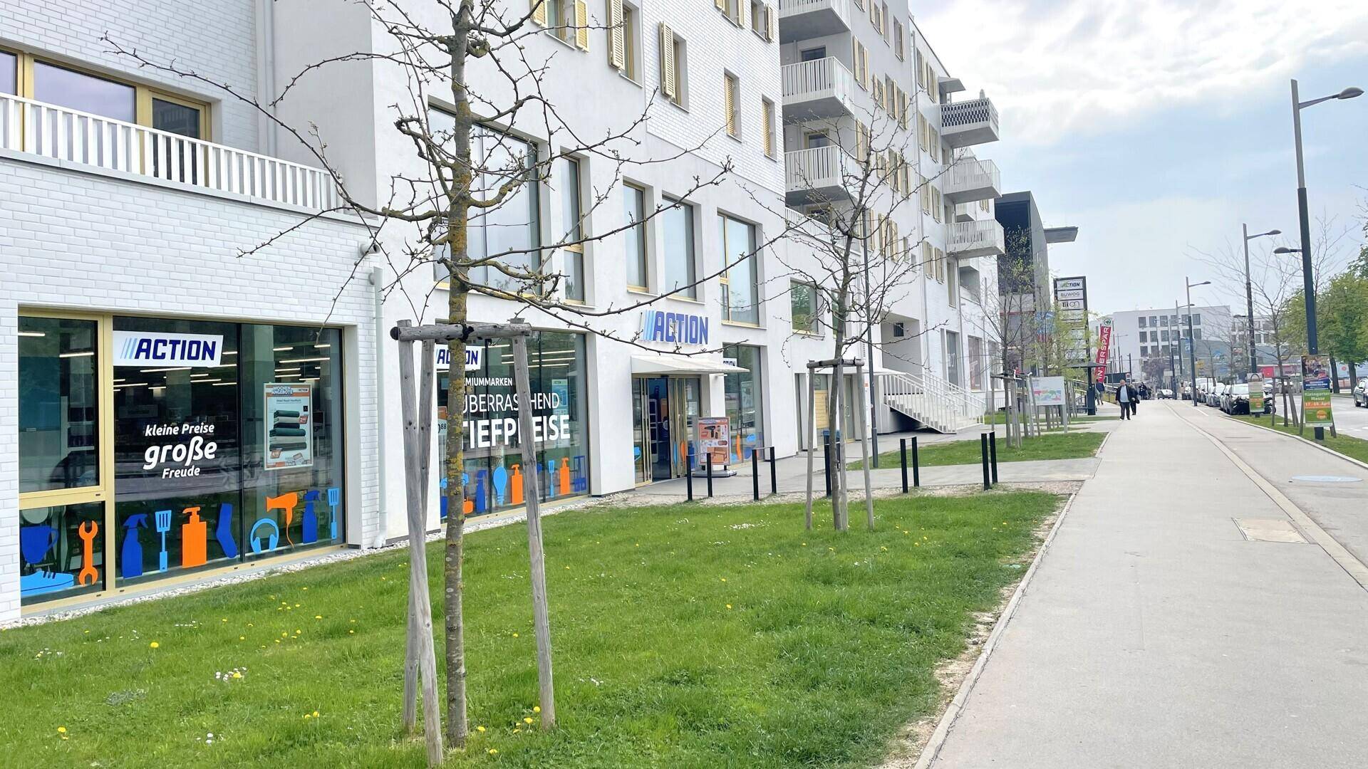 Moderne Geschäftsfassade mit großen Schaufenstern und Grünstreifen entlang der belebten Straße.