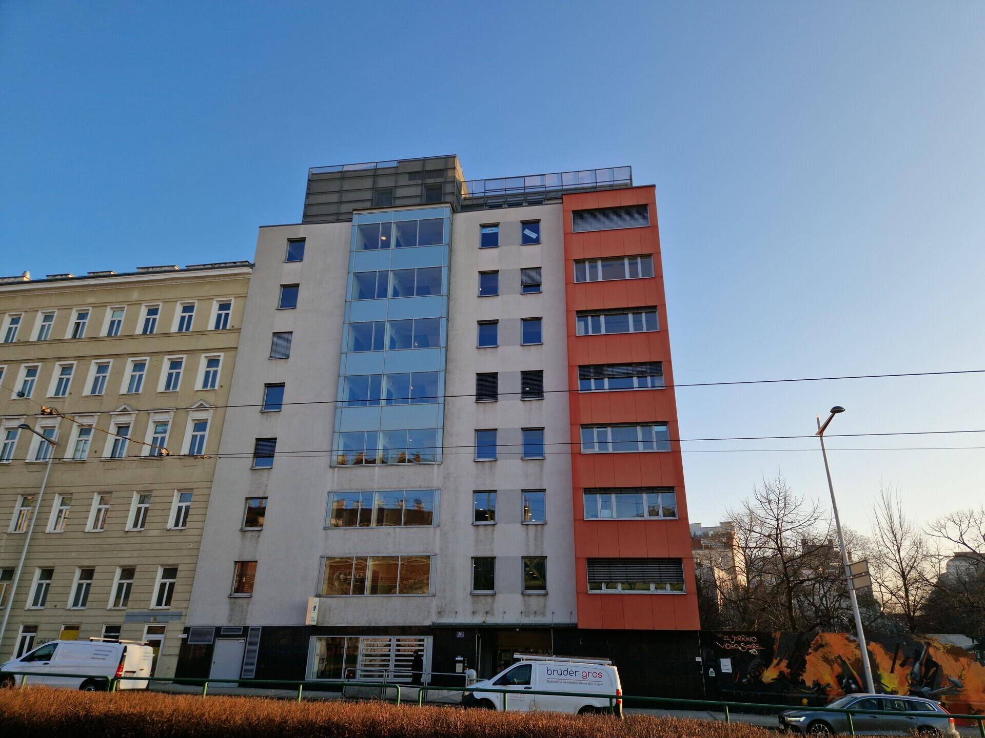 Ansicht des modernen Bürogebäudes mit markanten orangefarbenen Akzenten und großen Glasflächen unter blauem Himmel.