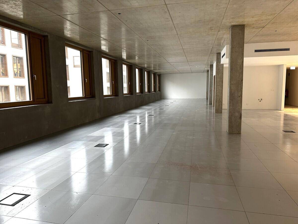 Langer, offener Bürobereich mit durchgehender Fensterfront und modernen Fliesenböden.