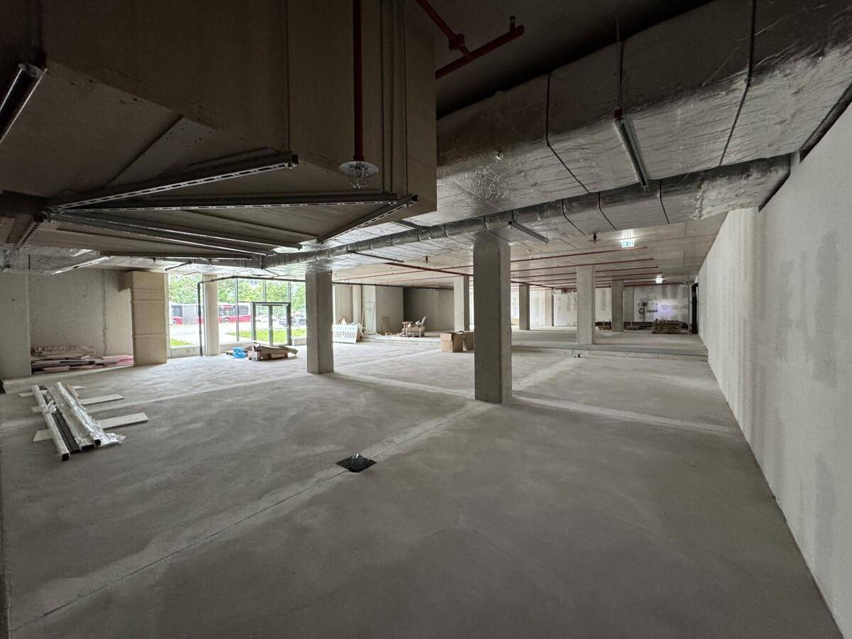 Ein großer, unfertiger Gewerberaum mit Betonboden, Säulen und sichtbaren Lüftungsrohren an der Decke.