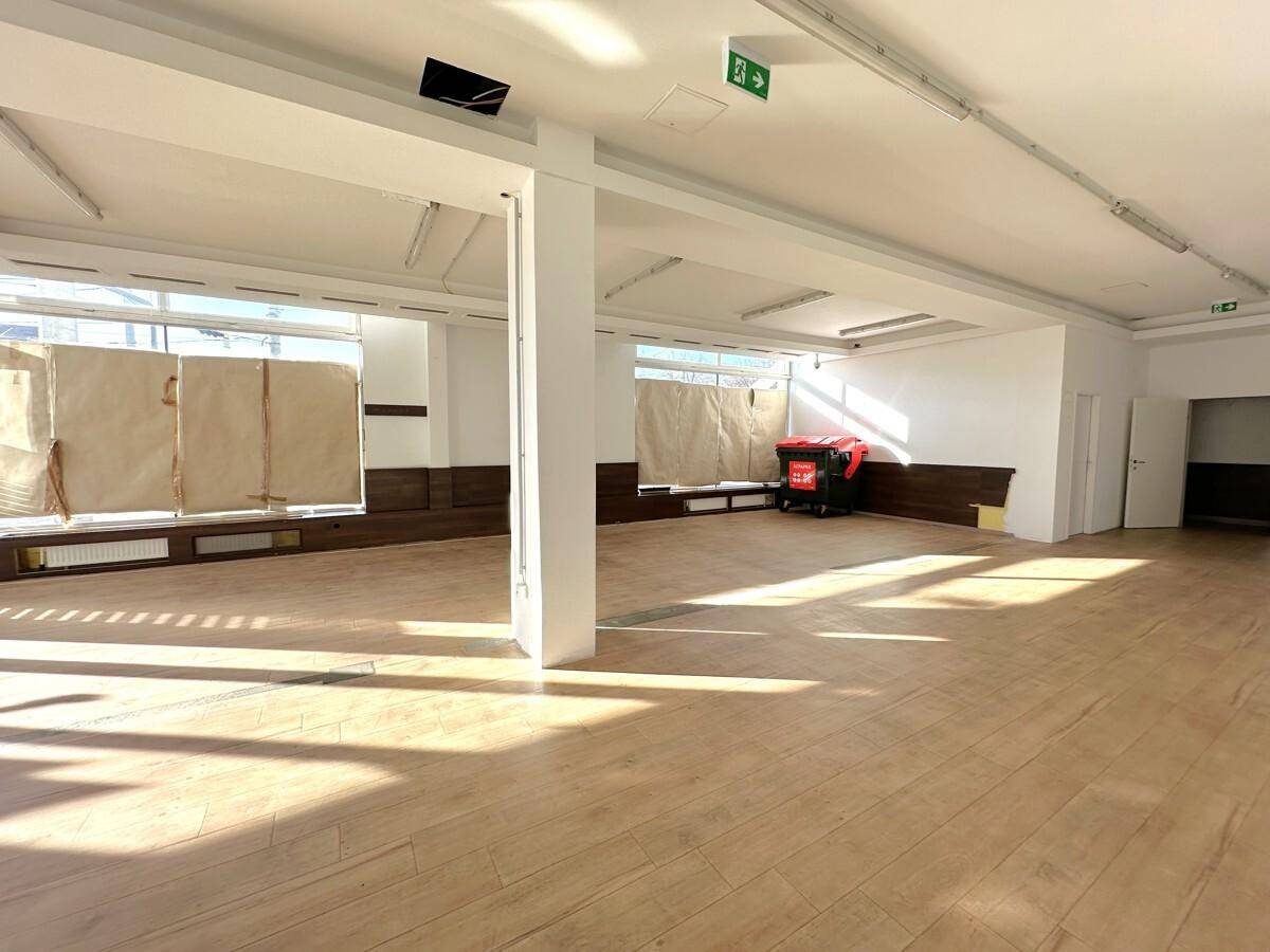 Heller, offener Verkaufsraum mit Holzboden, großen Fenstern und einer Holzvertäfelung an der Wand.