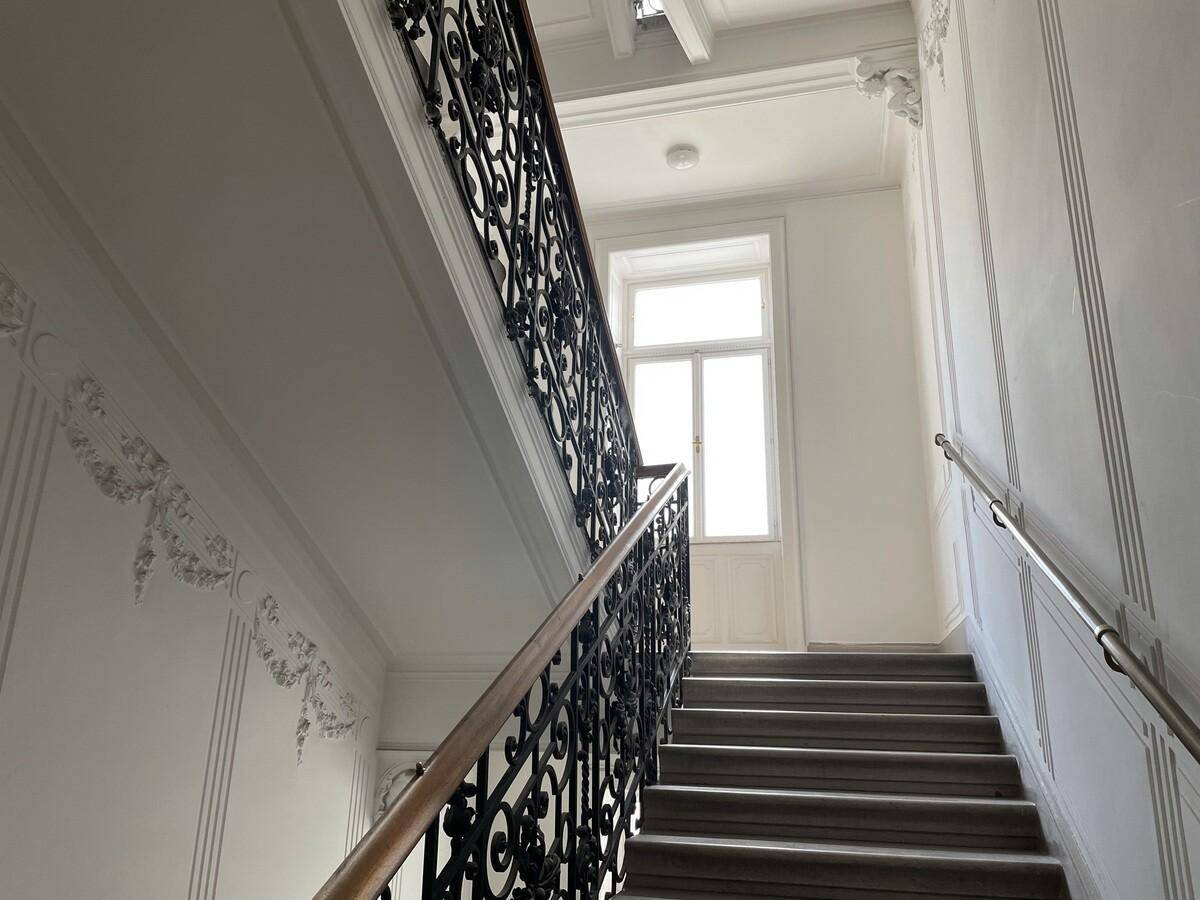 Historisches Treppenhaus mit kunstvollem schmiedeeisernem Geländer und einem Fenster, das Tageslicht spendet.