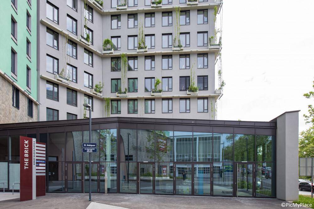 Moderner Eingangsbereich eines Gebäudes mit großer Glasfassade und Beschilderung an der Seite.