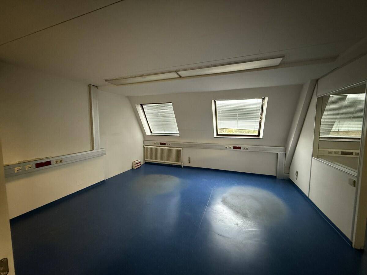 Büroraum im Dachgeschoss mit blauen Vinylböden, schrägen Wänden und Dachfenstern.