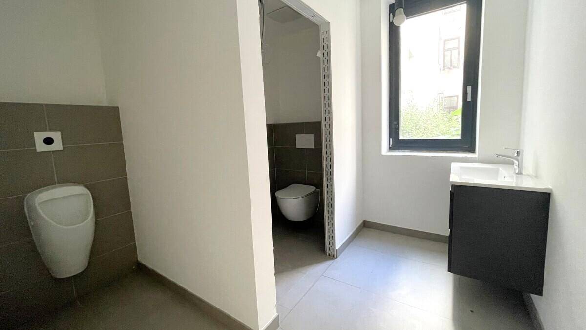 Modernes Badezimmer mit Urinal, Toilette, Waschbecken und Fenster für Tageslicht.
