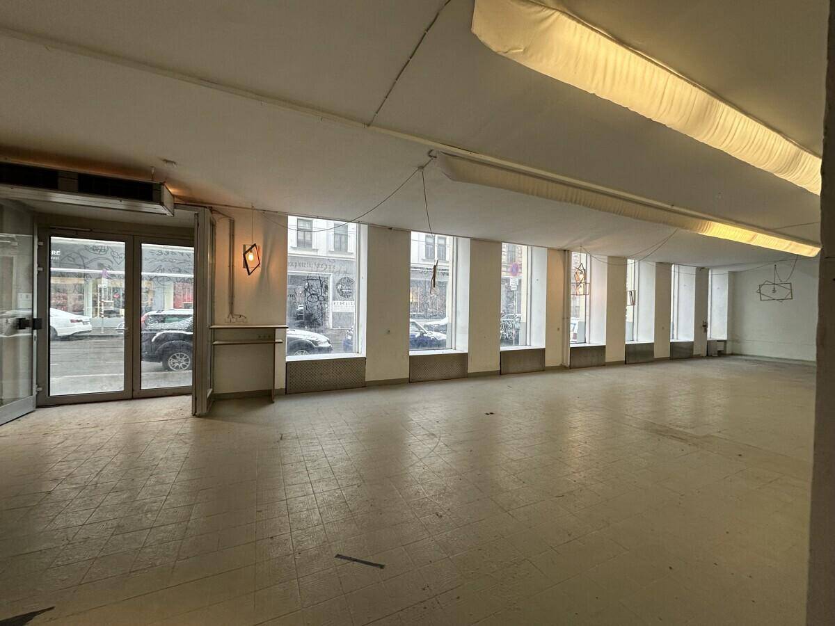Heller Gewerberaum mit gläsernen Eingangstüren und großen Schaufenstern, die zur Straße ausgerichtet sind.