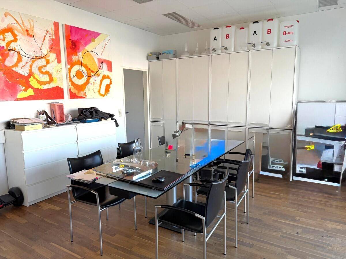 Moderner Besprechungsraum mit großem Glastisch, schwarzen Stühlen und weißen Schränken, dekoriert mit Kunstwerken.