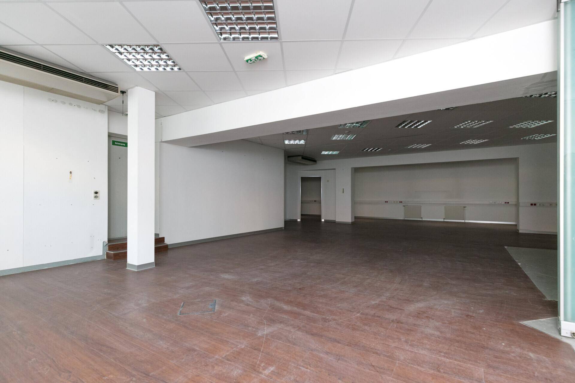 Weitläufiger Bürobereich mit Laminatboden, weißen Wänden und sichtbaren Versorgungskanälen.