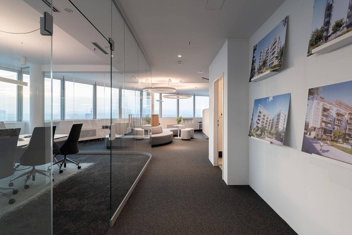 Heller Bürogang mit Glaswänden, Teppichboden und Bildern von Immobilien an der Wand.