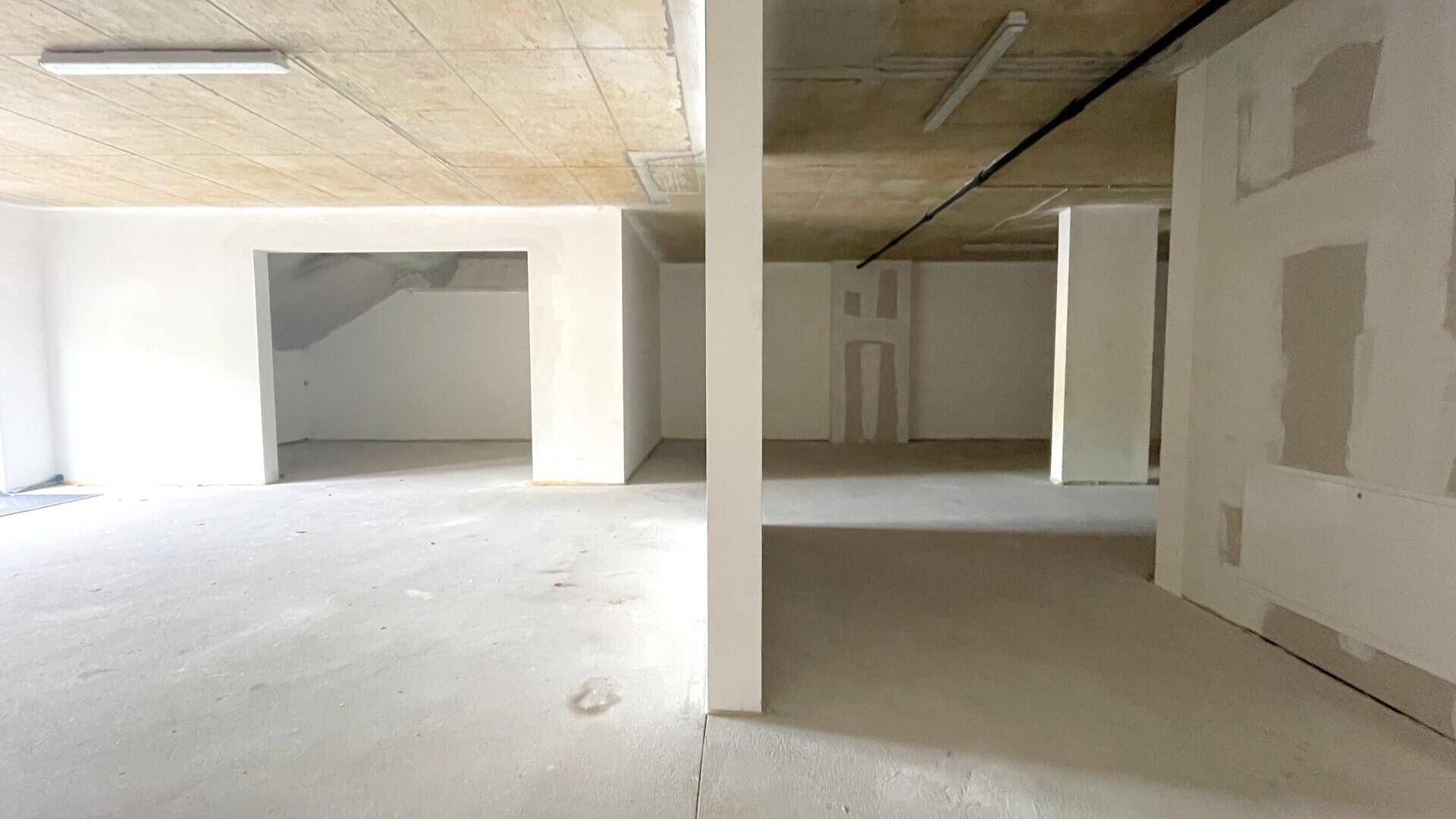 Weitläufiger, unfertiger Innenraum mit mehreren tragenden Säulen, Betonboden und -decke sowie einfacher Beleuchtung.