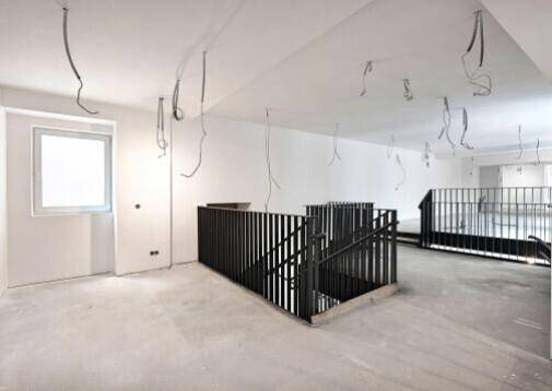 Heller Gewerberaum mit Betonboden, einem Fenster und der modernen schwarzen Treppe.
