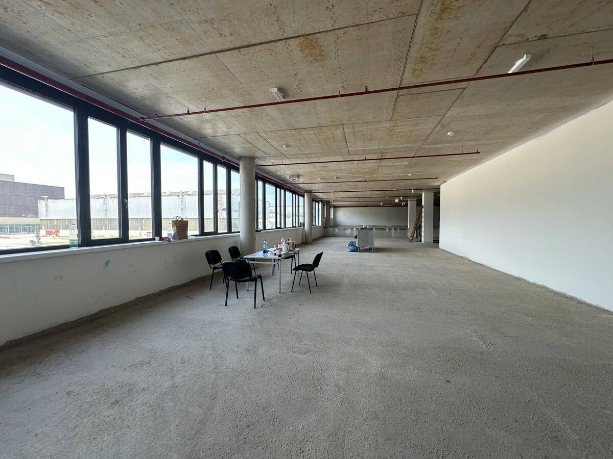 Weitläufiger Gewerberaum im Rohbauzustand mit durchgehenden Fensterfronten, die viel Licht spenden.