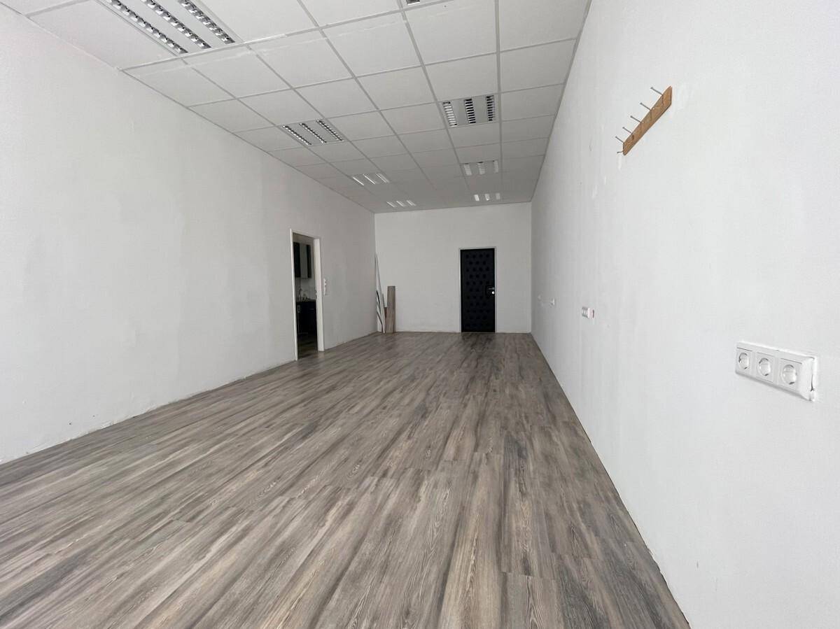 Langer, leerer Raum mit Laminatboden und weißen Wänden, im Hintergrund sind zwei Türen sichtbar.