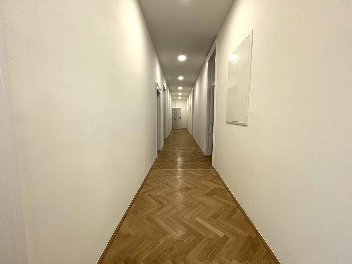 Langer, heller Flur mit Fischgrätparkett und mehreren Türen, beleuchtet durch Deckenspots.