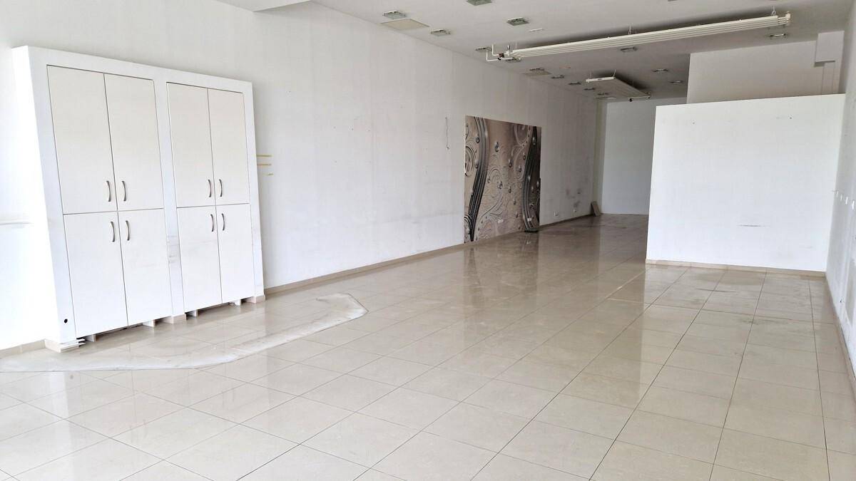 Geräumiger, leerer Ladenbereich mit hellen Fliesen, weißen Wänden und einem großen Schrank an der Wand.