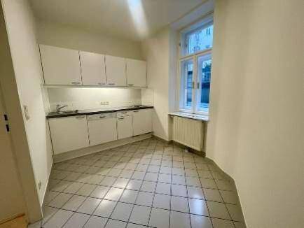 Funktionale Küche mit weißen Einbauschränken, Fliesenboden und einem Fenster für Tageslicht.