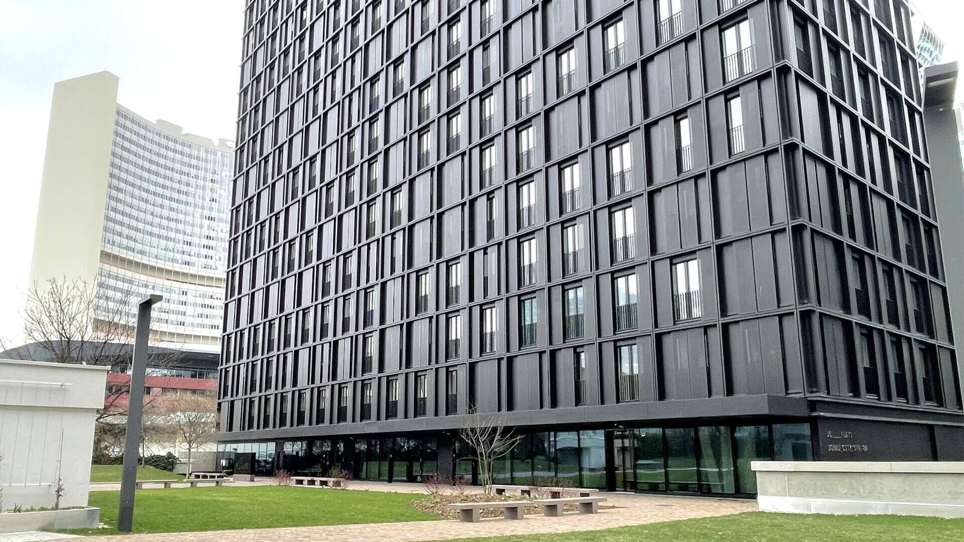 Detailansicht des modernen Hochhauses mit dunkler Fassade und großen Fenstern, umgeben von einer gepflegten Grünfläche.