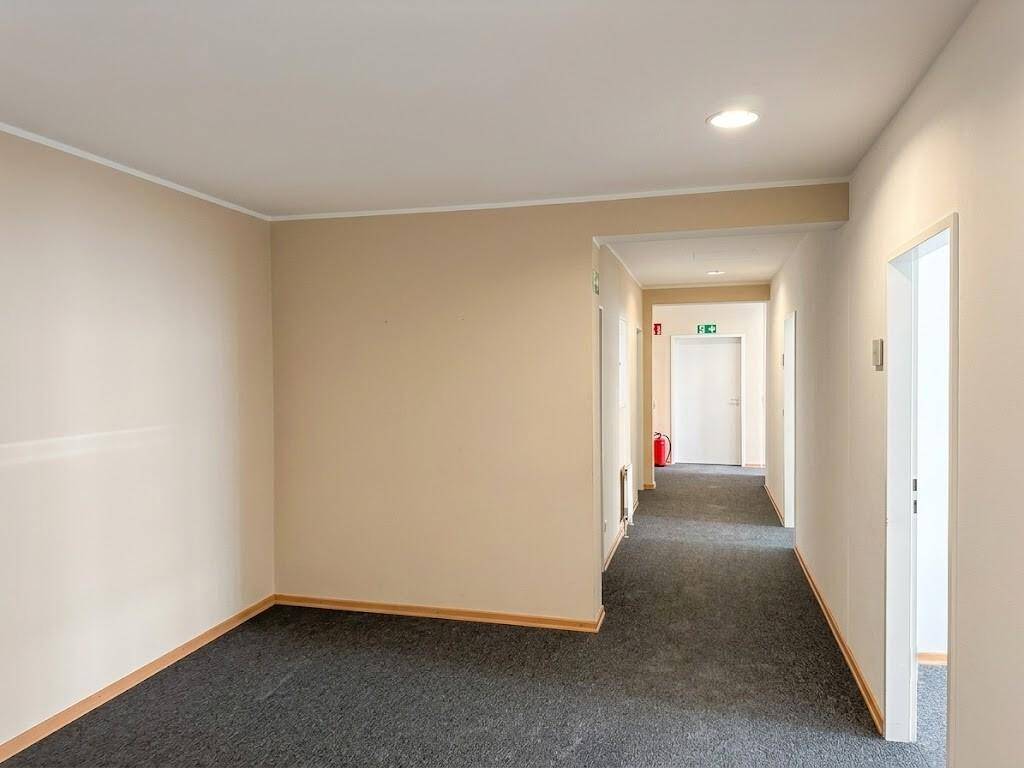 Heller Flur mit Teppichboden und beigen Wänden, der Zugang zu verschiedenen Büroräumen bietet.