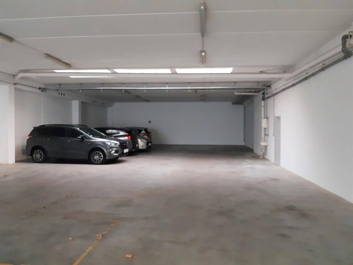 Geräumige Tiefgarage mit mehreren parkenden Autos, Betonboden und Deckenbeleuchtung für gute Sicht.