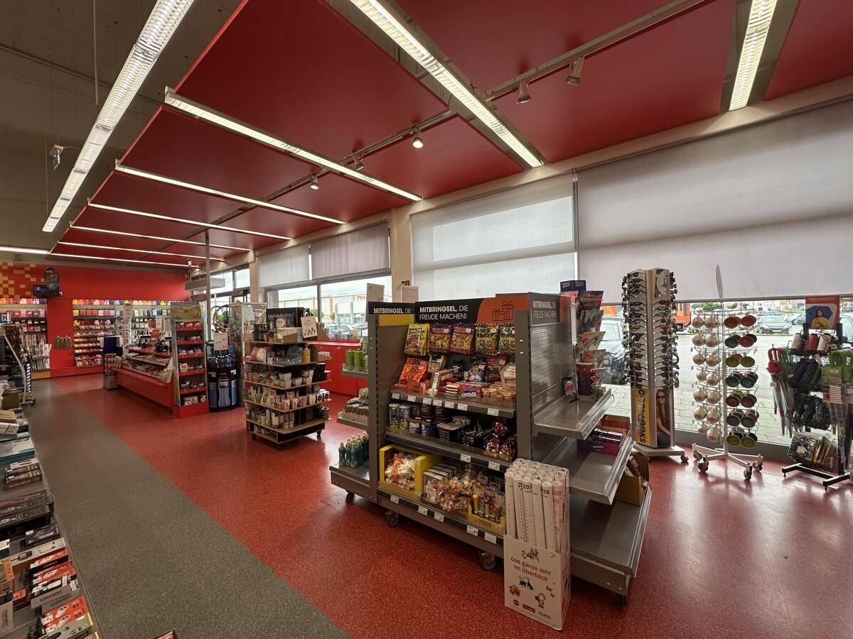 Verkaufsbereich mit rotem Boden und passenden Deckenpaneelen, großen Fenstern und Produktregalen.