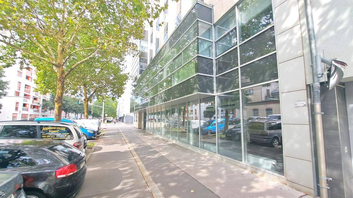 Lange Glasfassade eines modernen Gebäudes entlang der Straße mit geparkten Autos.