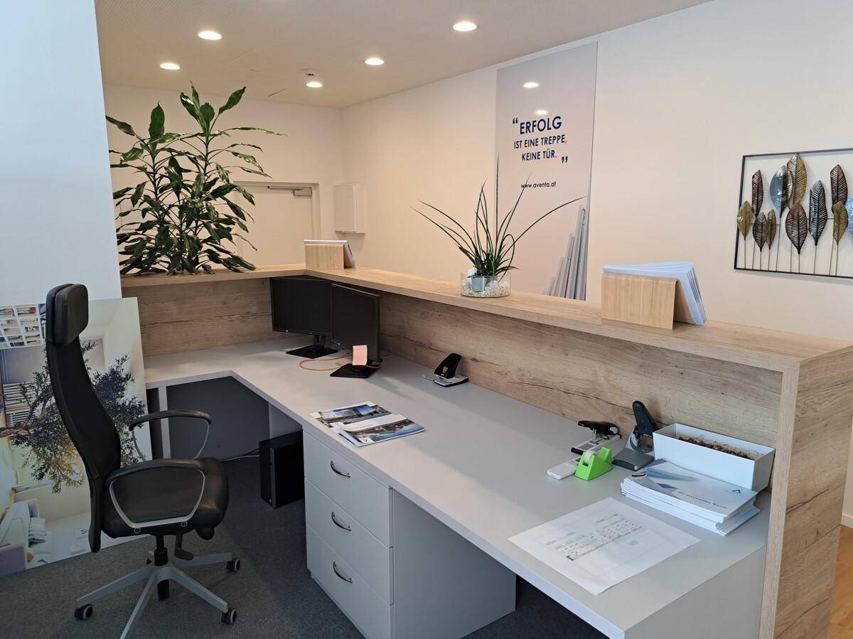 Moderner Bürobereich mit Holztheke, Arbeitsplätzen und Pflanzen als Dekoration.