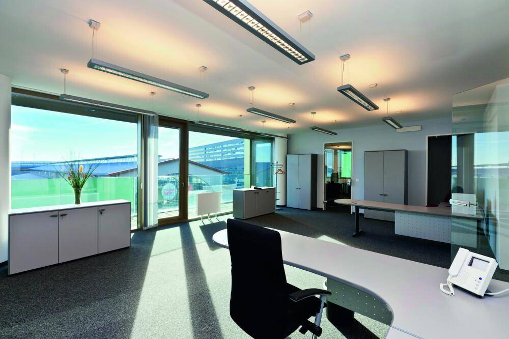 Modern eingerichtetes Büro mit Schreibtischen, Bürostühlen und großen Fenstern für viel Tageslicht und Ausblick.